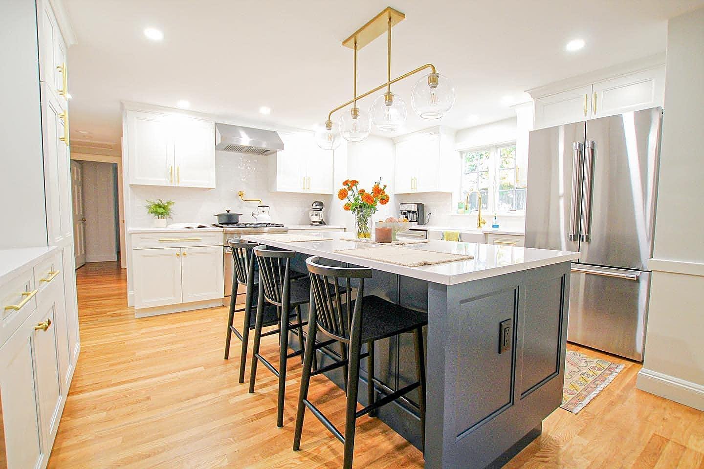 A finished kitchen with a navy island, brass pulls, white cabinets and oak floors